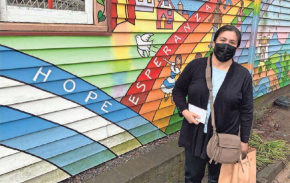 a woman wearing a mask standing next to a colorful mural on the side of a building